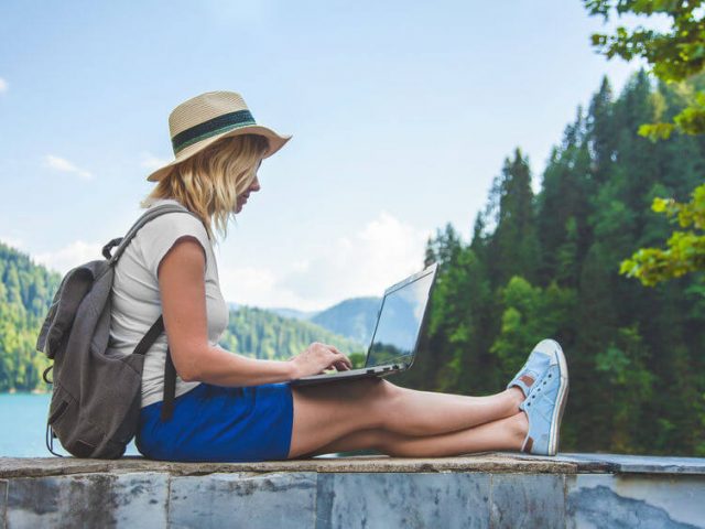 women with laptop and backpack sit in outside - travel concept