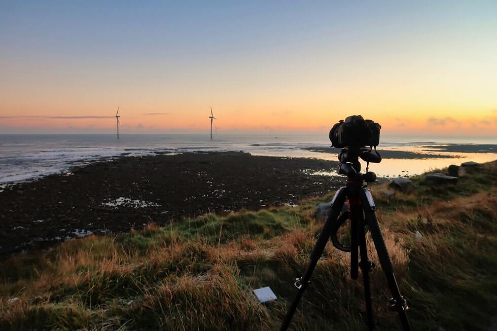 black camera with tripod near body of water