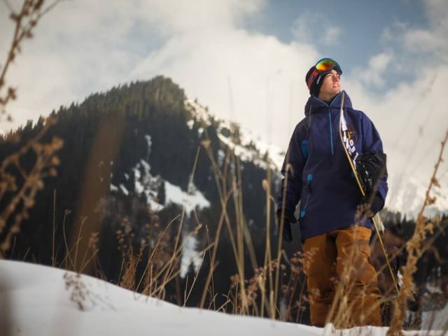 man wearing blue hardshell jacket and carrying snow board