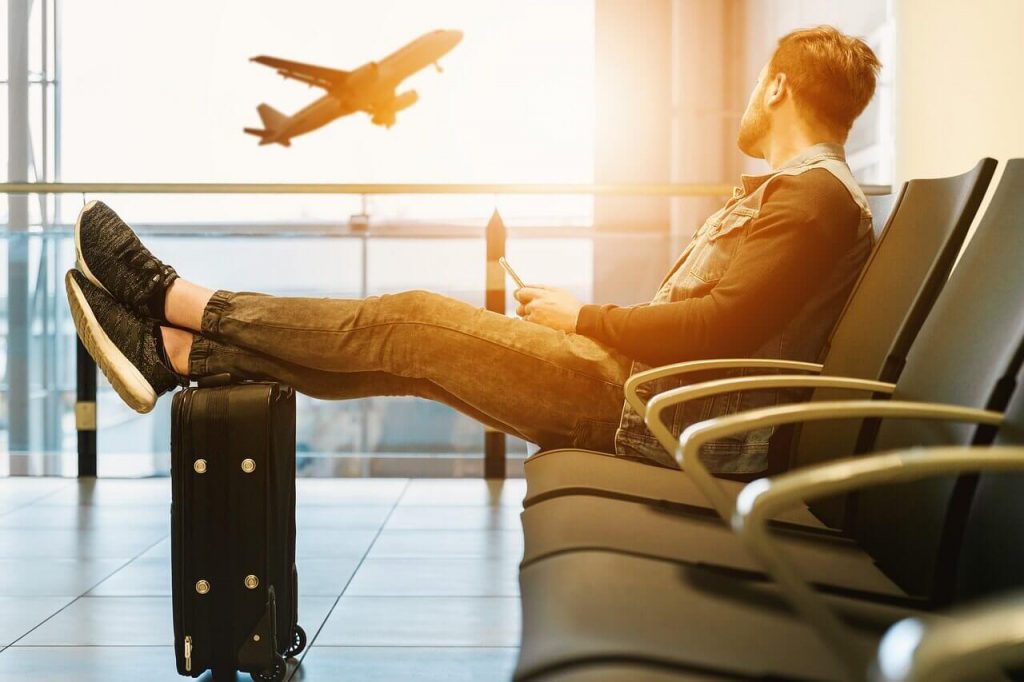 man siting in airport terminal with wheeled carry-on backpack