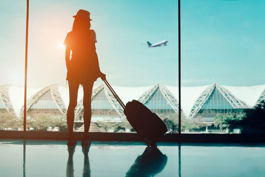 woman with wheeled travel backback looking window at airport terminal